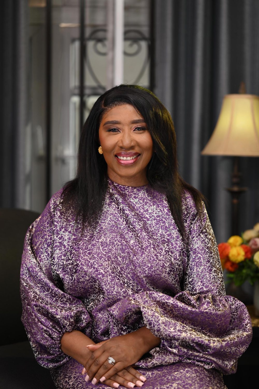 Bukky Onifade smiling, seated in a purple patterned top in a softly lit room